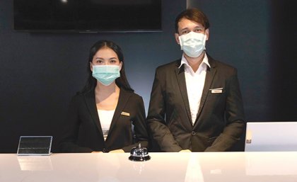 A woman and a man wearing dark suits standing behind a counter in masks